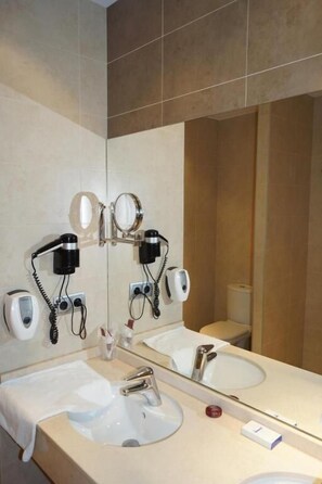 Un baño con dos lavamanos, un espejo grande y secadores de pelo montados en la pared.