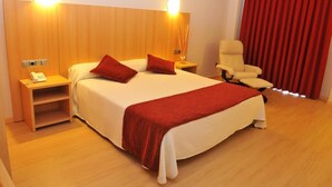 Una habitación de hotel con una cama grande, dos mesitas de noche, una silla y una cortina roja.