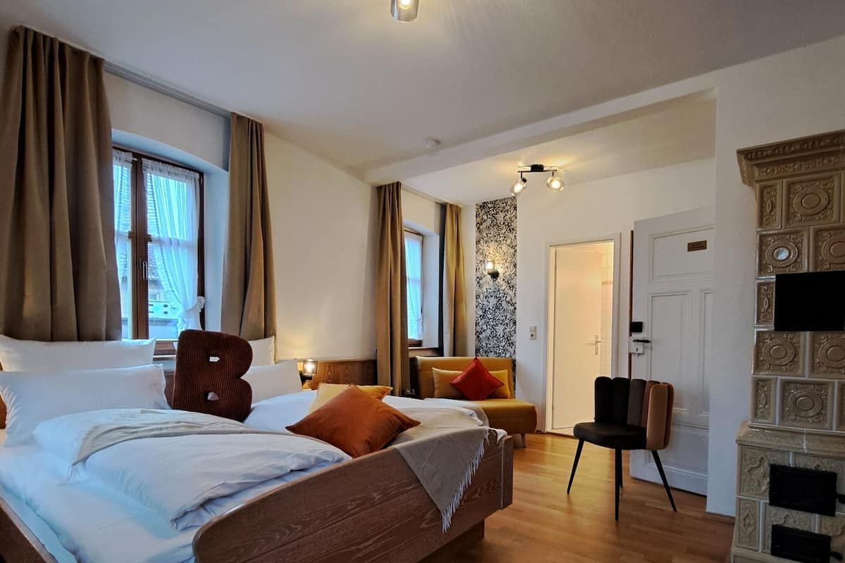 A spacious bedroom with a large bed, a wooden floor, a fireplace, and a view of the outdoors.