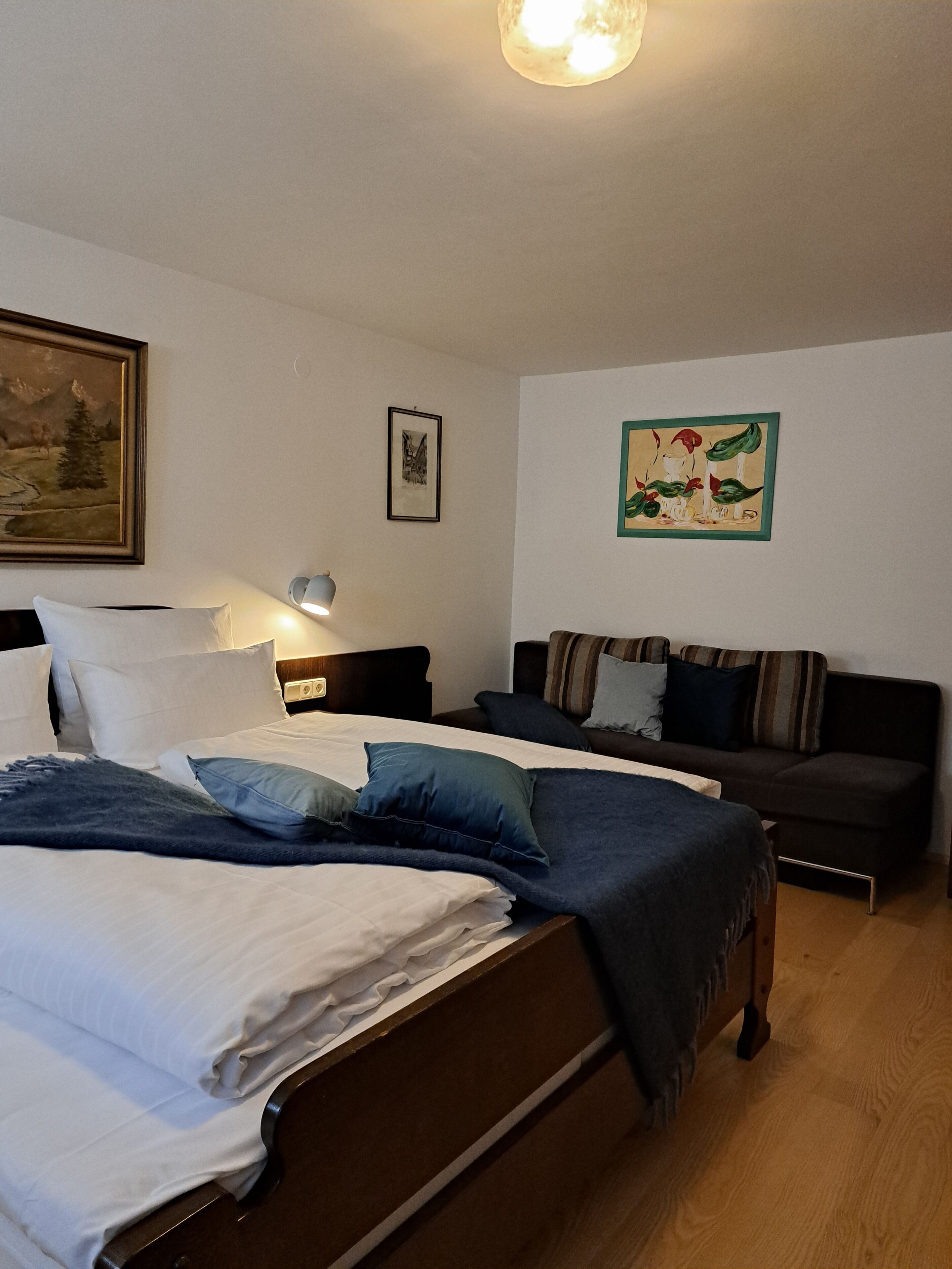 Un dormitorio con cama, mesita de noche, lámpara y un sofá.