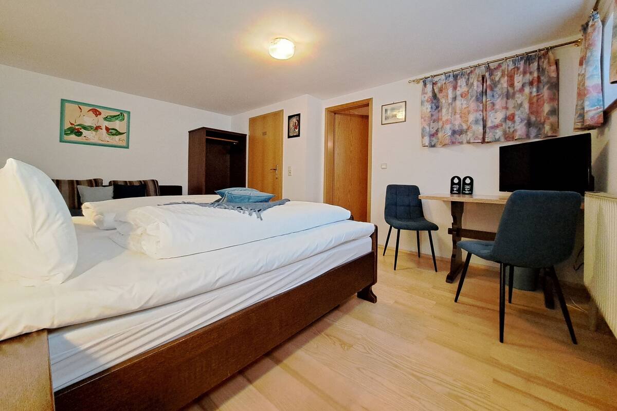 A bedroom with a bed, a desk, two chairs, a television, and a door.