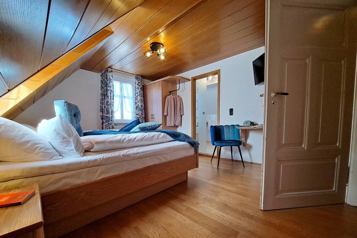A bedroom with a lofted ceiling, a bed with pillows, a chair, and a desk.