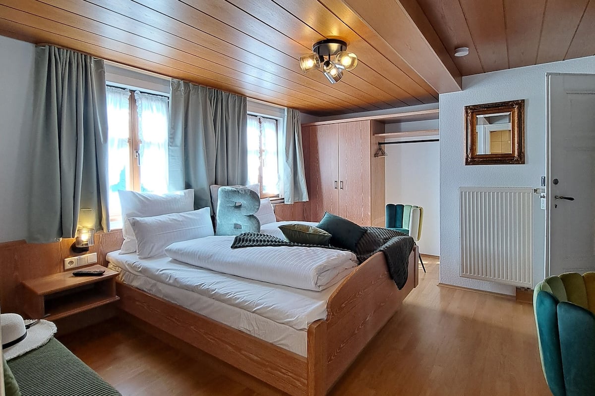 A wooden-paneled bedroom with a bed, bedside table, lamp, and a chair.