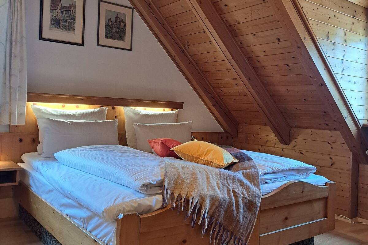 A wooden bed in a room with a sloped ceiling and framed pictures on the wall.