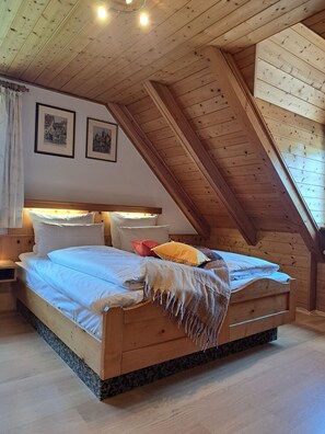 A wooden bed in a room with a sloped ceiling and framed pictures on the wall.