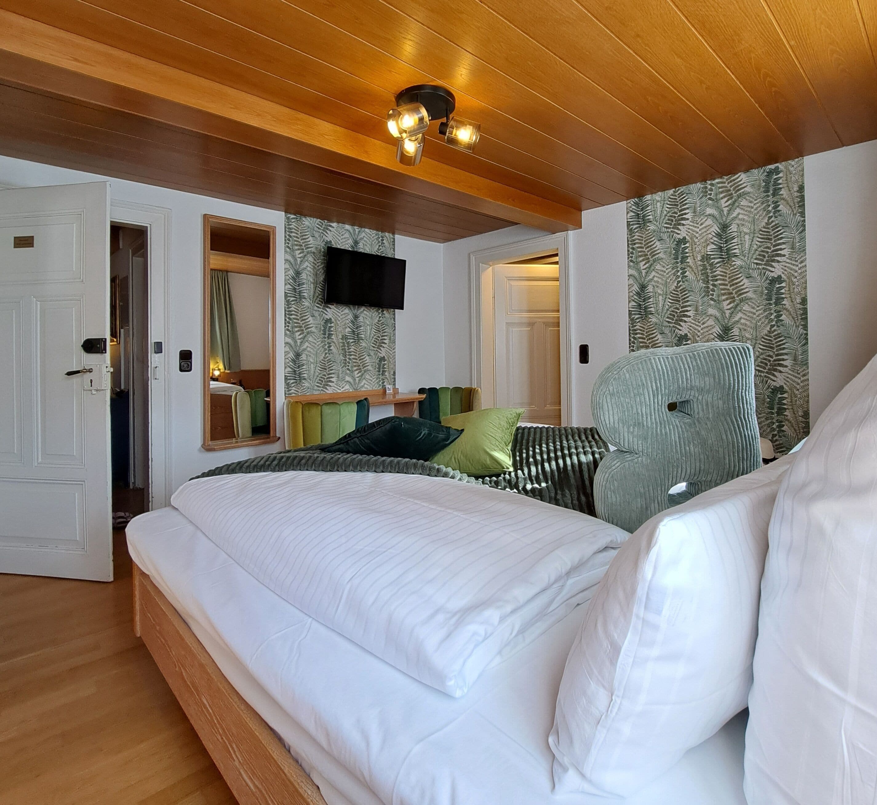 A bedroom with a bed, a television mounted on the wall, and a wooden ceiling.