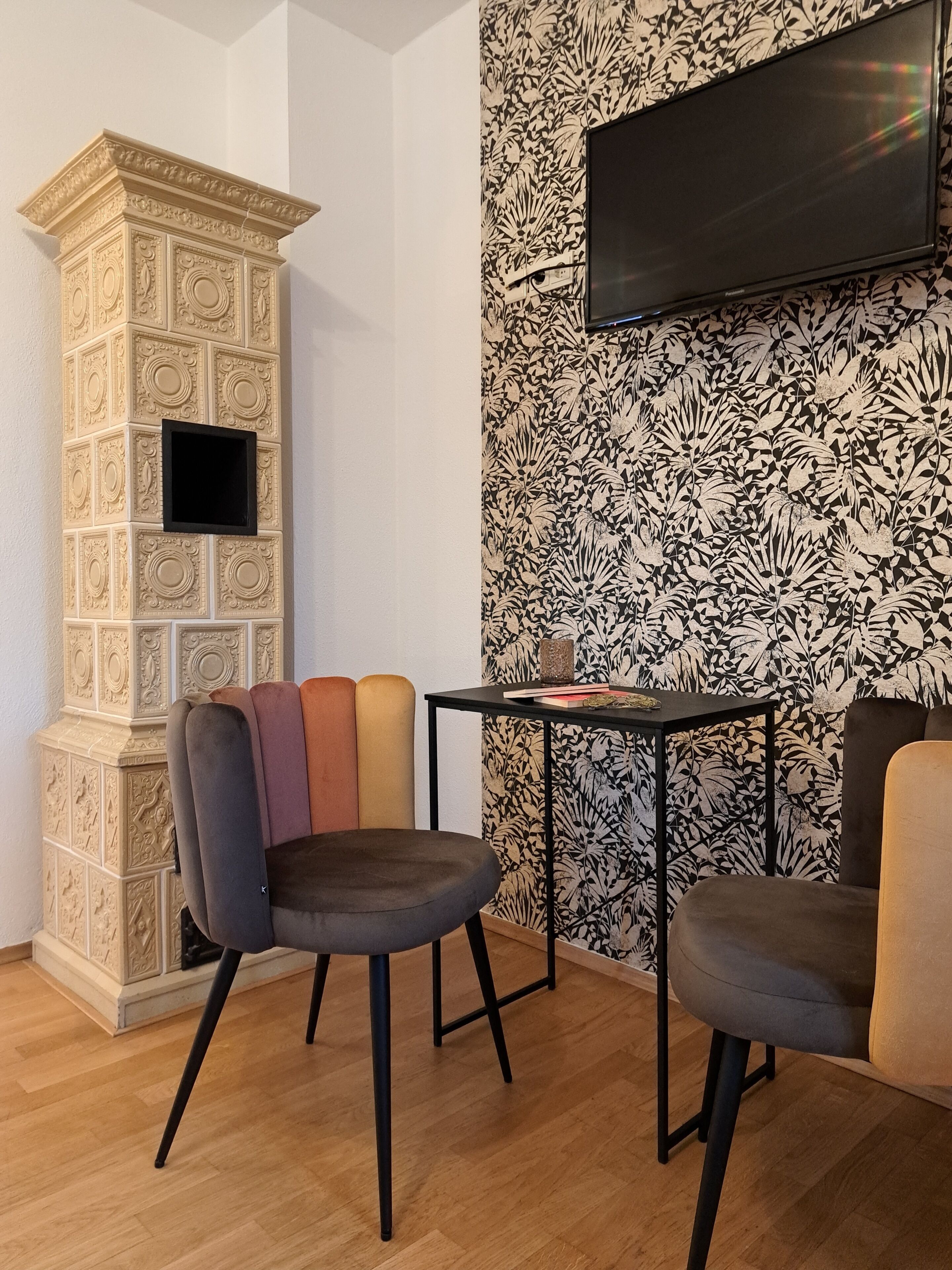 A room with a decorative column, a flat-screen TV mounted on the wall, and a patterned wallpaper.