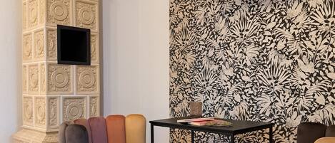 A room with a decorative column, a flat-screen TV mounted on the wall, and a patterned wallpaper.