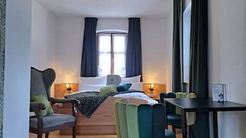 Una habitación de hotel con cama, escritorio, silla, ventana con cortinas e iluminación en el techo.