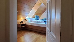 A bedroom with a sloped ceiling, a bed, a nightstand, and a desk with a lamp. - Gasthof Hotel Bezold (Rothenburg ob der Tauber)