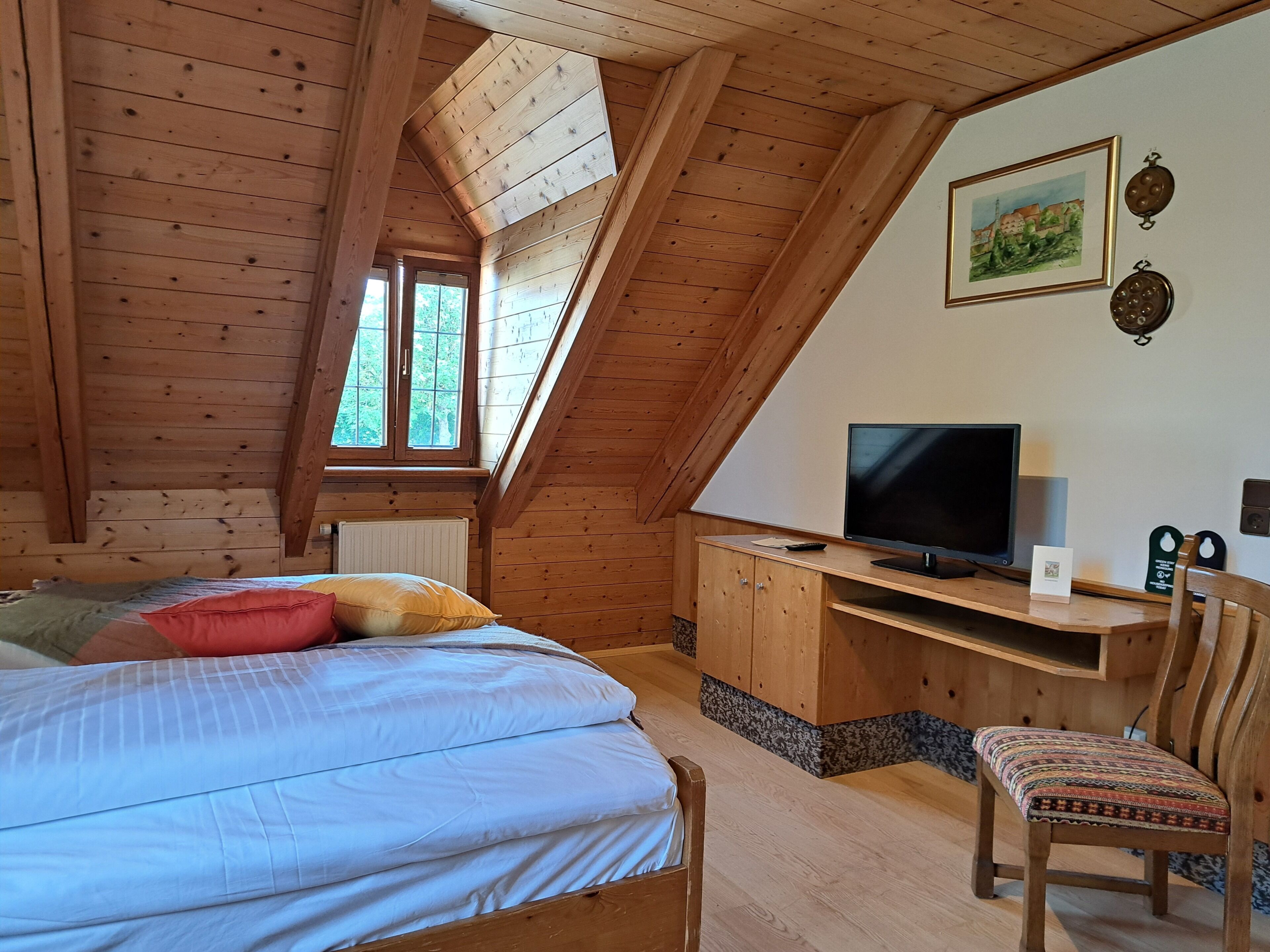 A wooden room with a bed, a desk with a TV, and a chair.