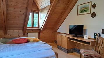 A wooden room with a bed, a desk with a TV, and a chair.