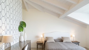Une chambre avec un plafond en pente, un lit avec deux oreillers, des tables de chevet avec des lampes et un mur orné d’un motif géométrique.