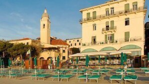 Une zone de plage avec des rangées de chaises longues vertes et un bâtiment surmonté d’une tour en arrière-plan.