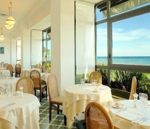 Un restaurante con mesas redondas, sillas y vistas al océano.