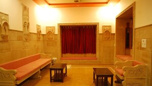 A room with two ornate sofas, a small table, and a red curtain. - Ratnawali (Jodhpur)
