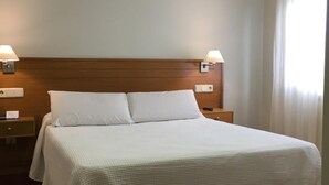 A neatly made bed with a wooden headboard, two bedside tables with lamps, and a window with curtains. - Hotel Arteixo (Arteixo)