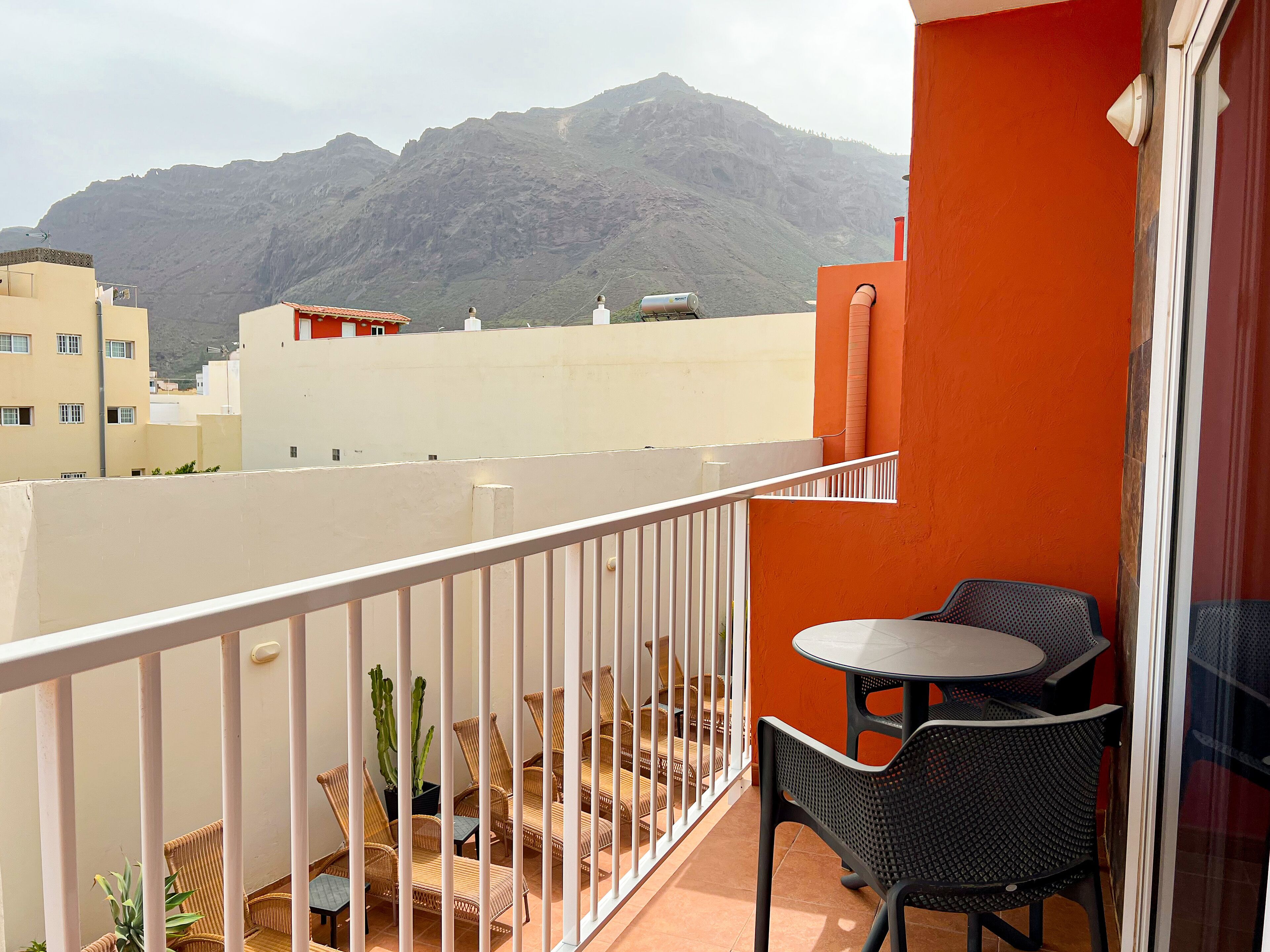A balcony with a table and chairs, a cactus plant, and a view of mountains in the background.