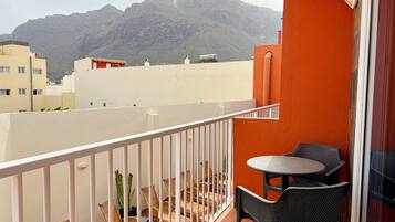 A balcony with a table and chairs, a cactus plant, and a view of mountains in the background.