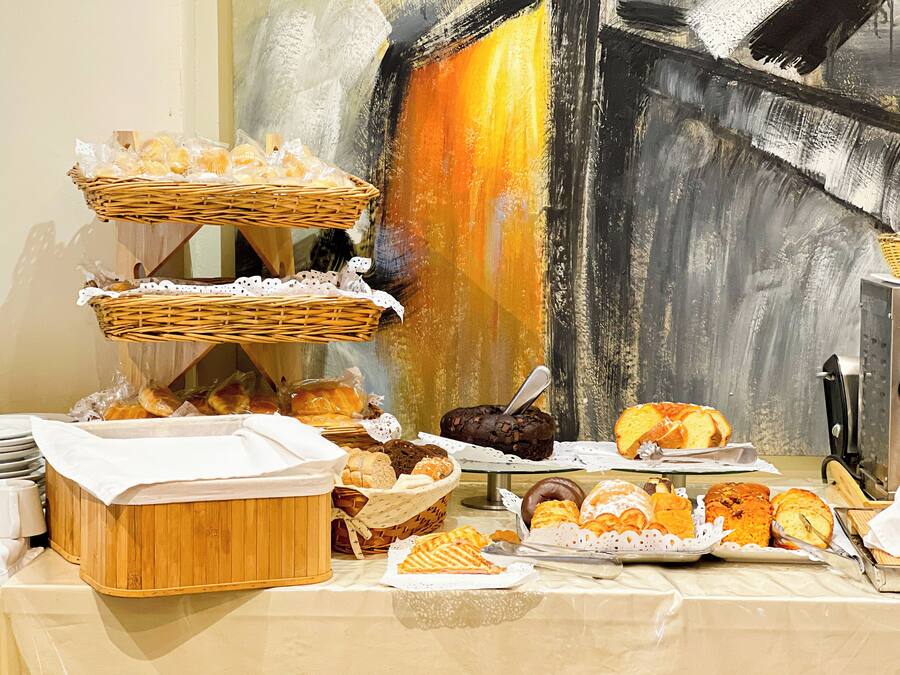 Una mesa de buffet con diversos productos de pastelería y repostería, incluyendo pan, pasteles y galletas, dispuestas sobre un mantel blanco.