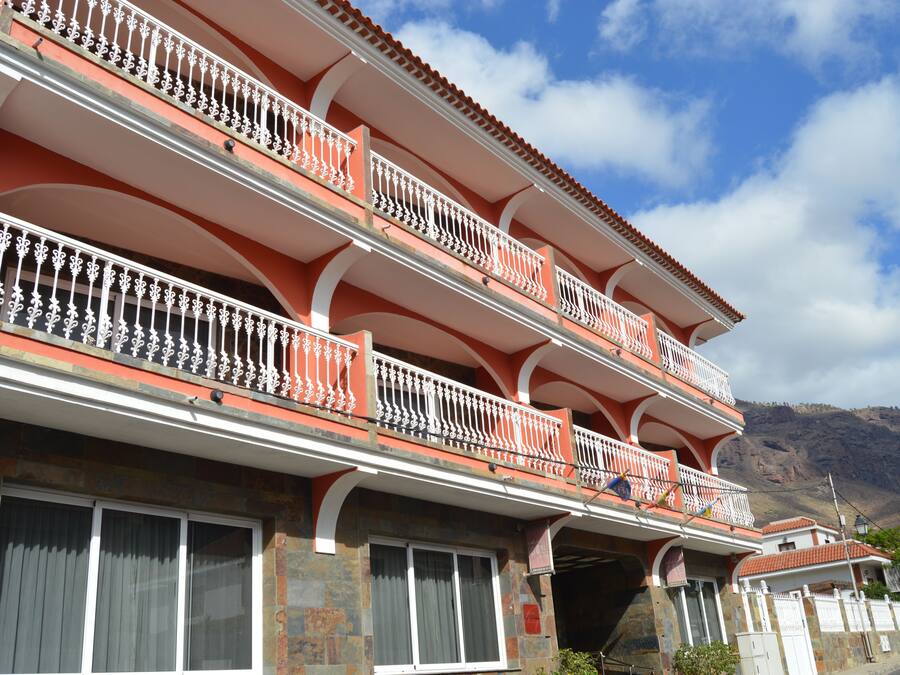 A multi-story building with balconies, stone facade, and a mountainous backdrop.
