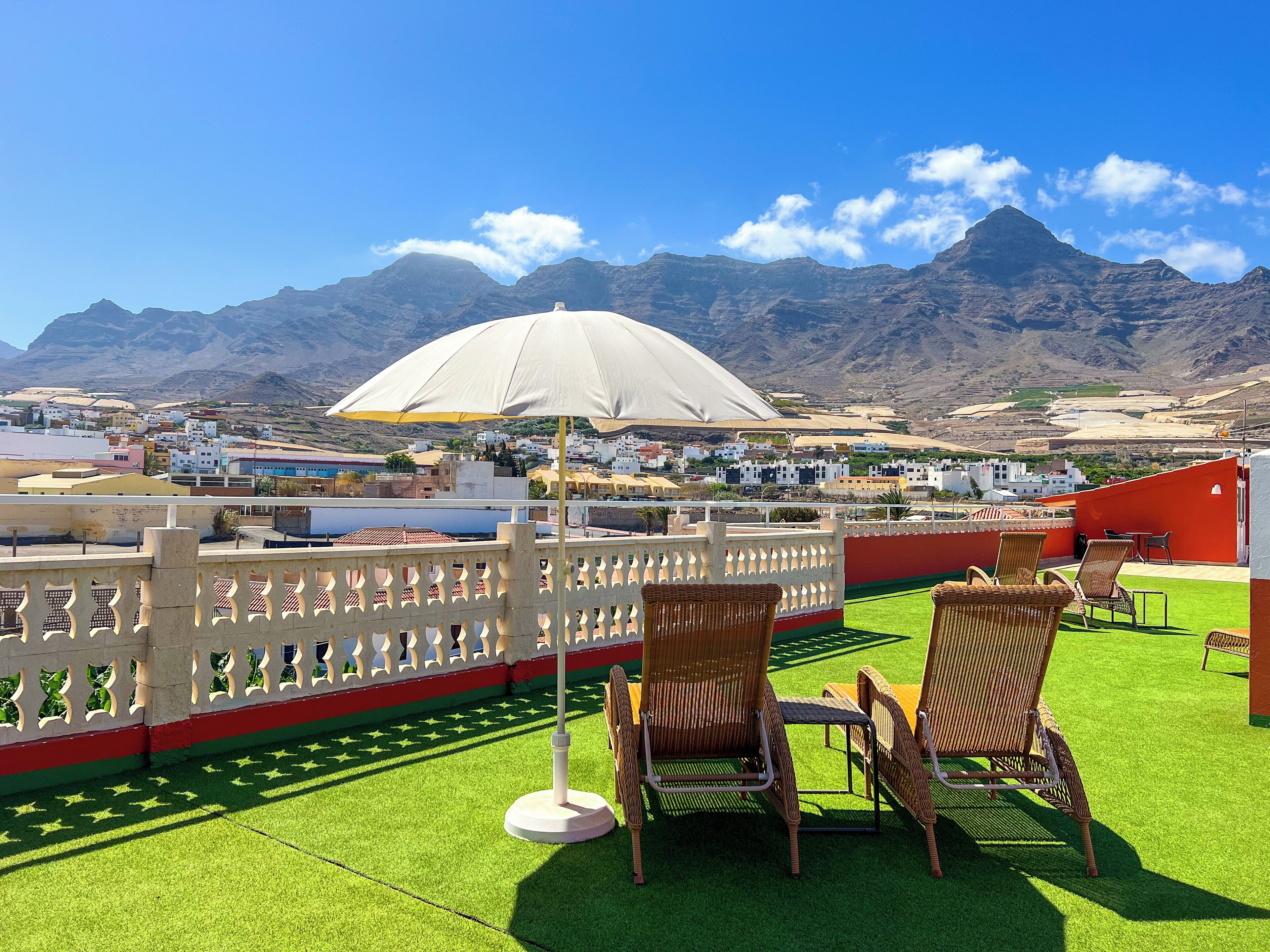 Une terrasse dotée de chaises en osier et d’un grand parasol, offrant une vue sur la ville et les montagnes.