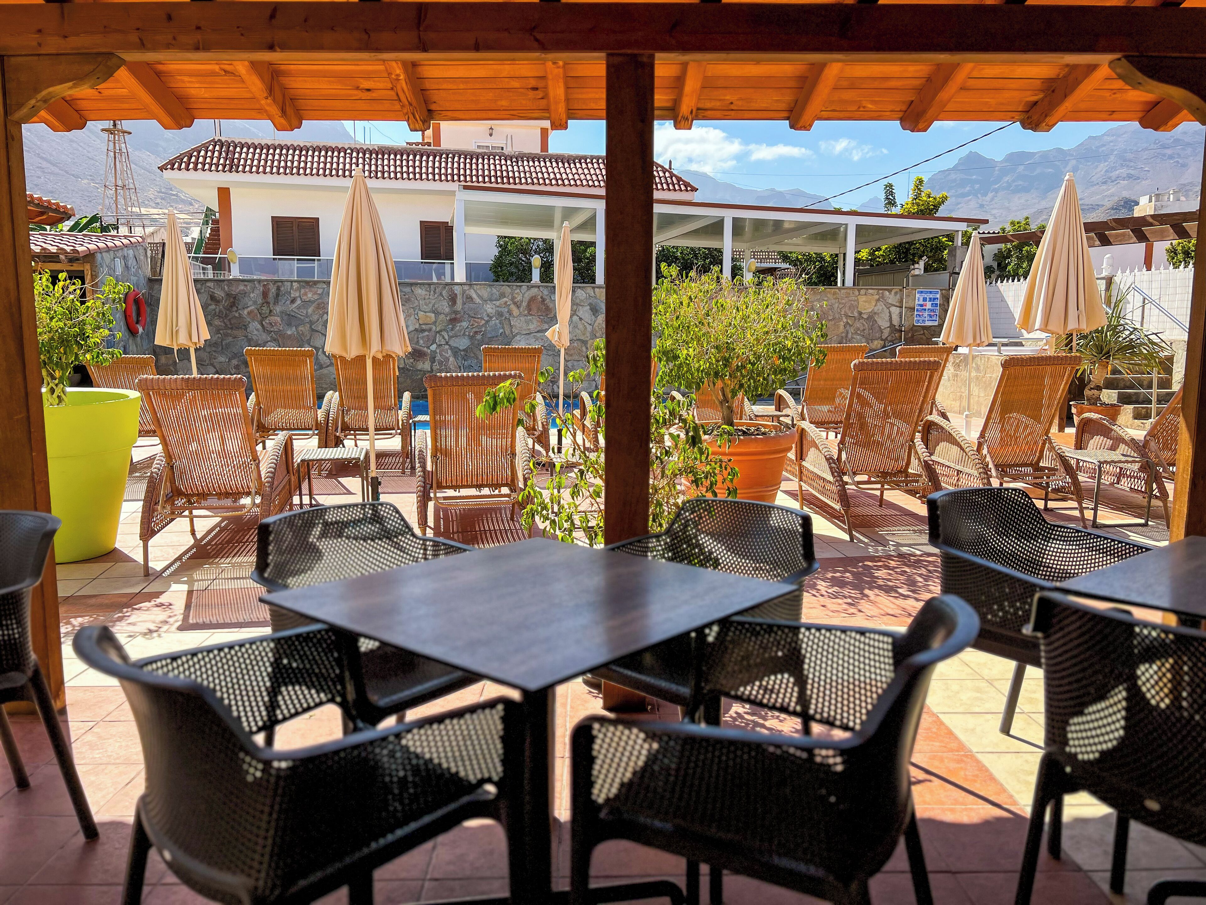 An outdoor patio with wicker chairs and tables, umbrellas, and potted plants.
