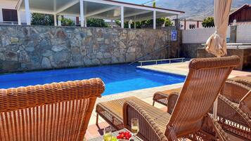 A pool area with wicker furniture and a table with fruit and a glass of wine.