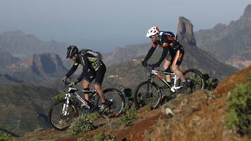 Dos ciclistas en un sendero de bicicleta de montaña, con montañas al fondo.