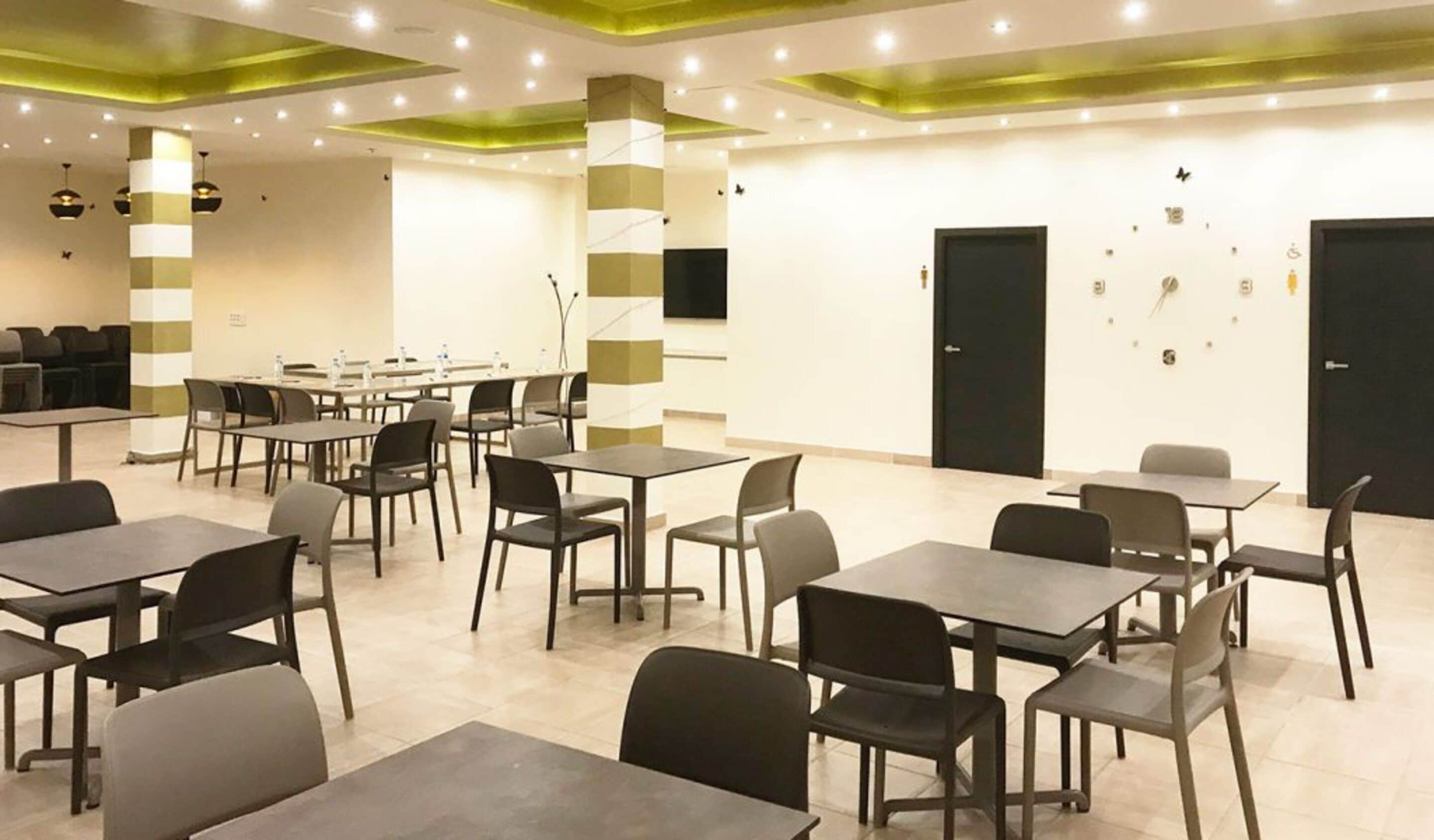 Un salón de conferencias con mesas y sillas, iluminación de acento verde y una puerta negra.