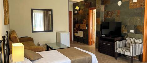 A hotel room with two beds, a television, a seating area with a striped chair, and a stone wall.