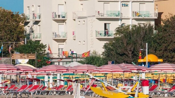 A hotel with multiple balconies, red and white striped beach umbrellas, and beach chairs. - Hotel Rivazzurra (Pesaro)