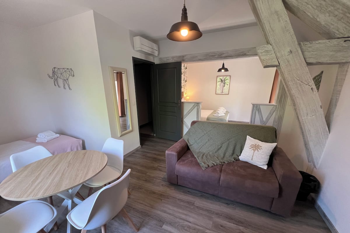 Une pièce chaleureuse avec une table à manger en bois, des chaises blanches, un canapé marron avec un plaid et un plafond en bois.