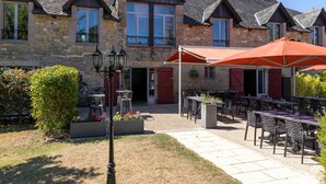 Un bâtiment en pierre doté d’une cour, d’un espace extérieur aménagé avec des sièges et d’un parasol rouge.