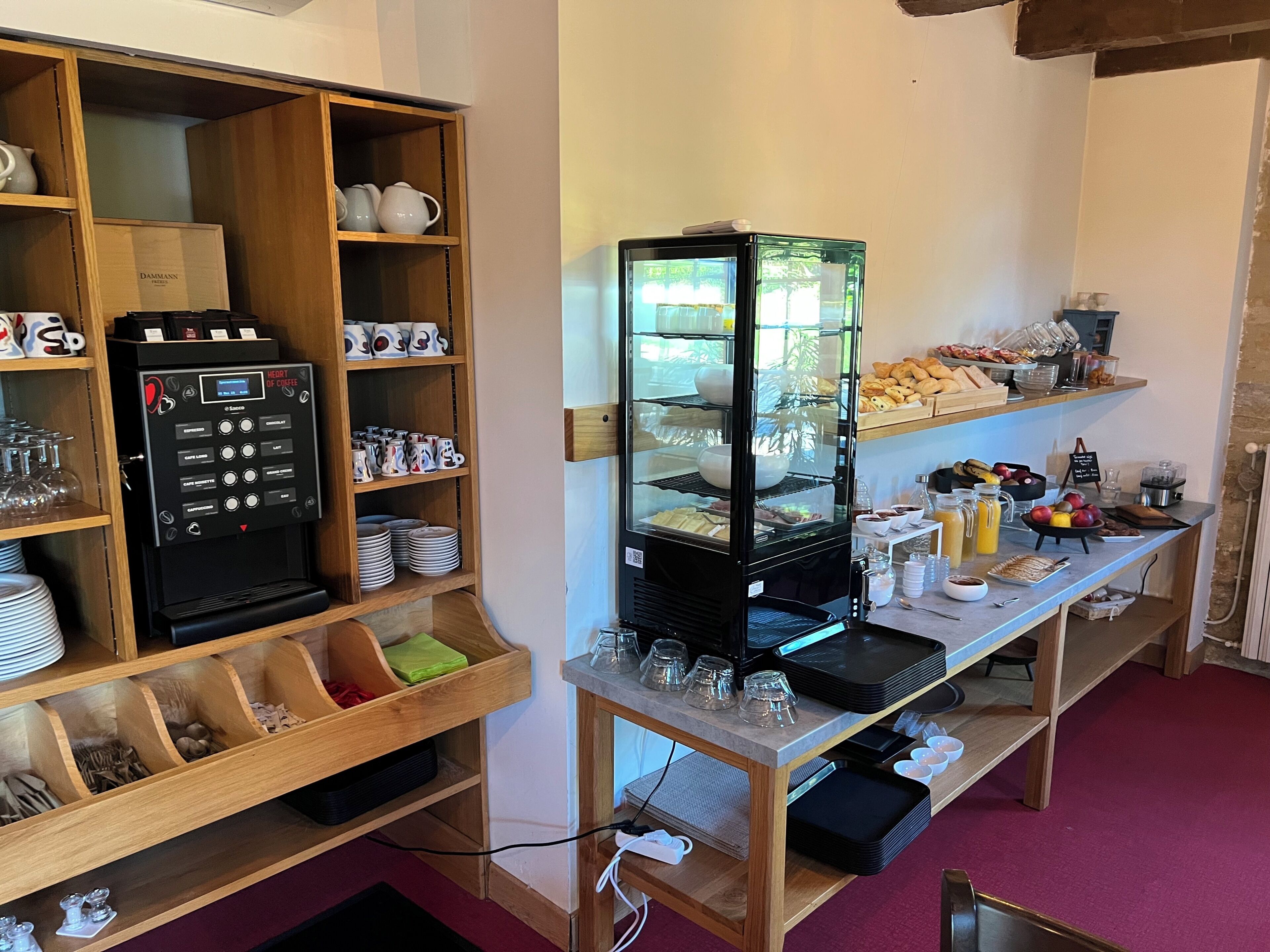 A coffee station with a coffee machine, glassware, and a display case with food items.