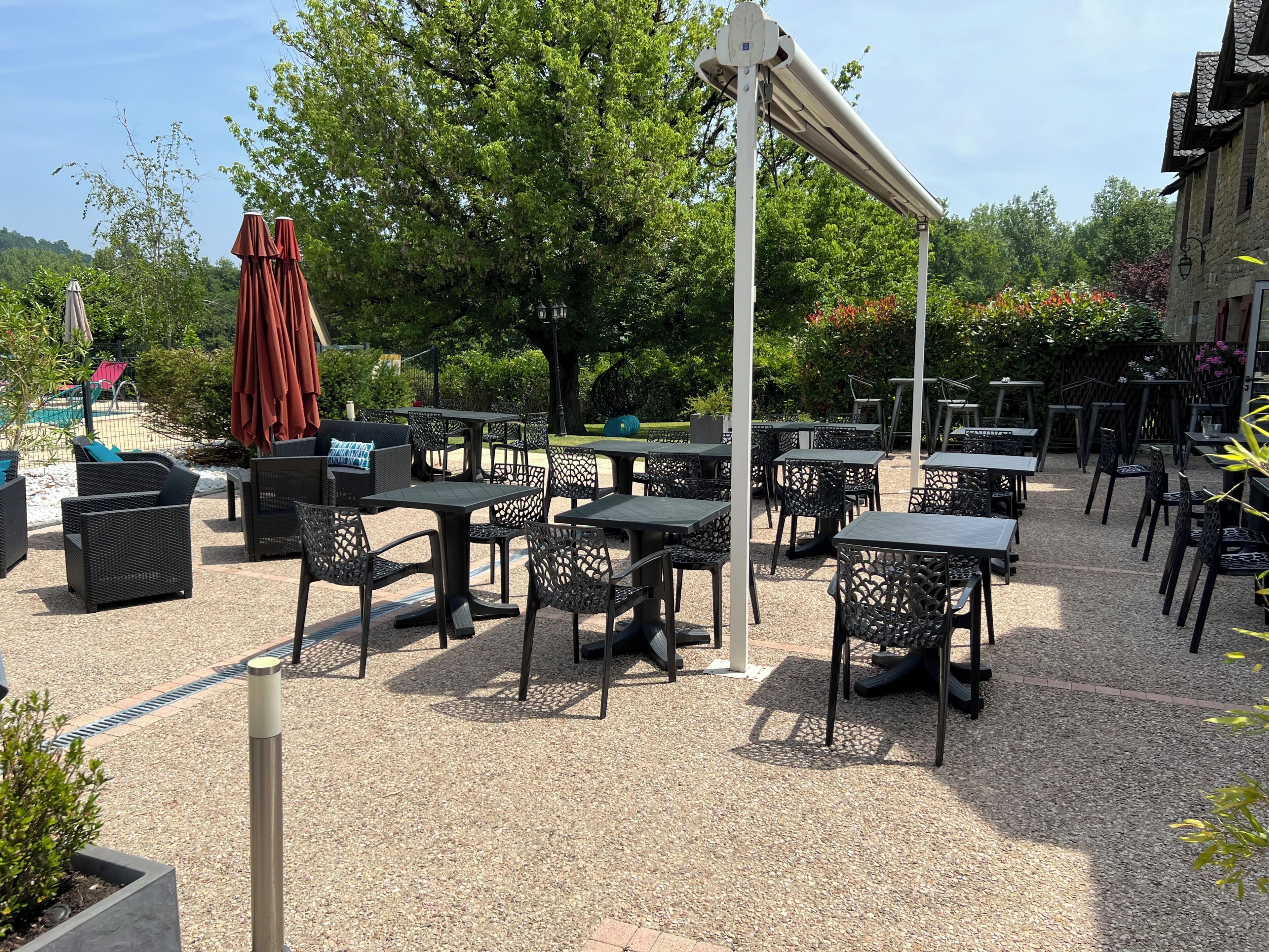 An outdoor patio area with tables and chairs, surrounded by trees and a pool.