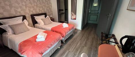 A hotel room with two beds, a desk, a chair, and a kitchenette.