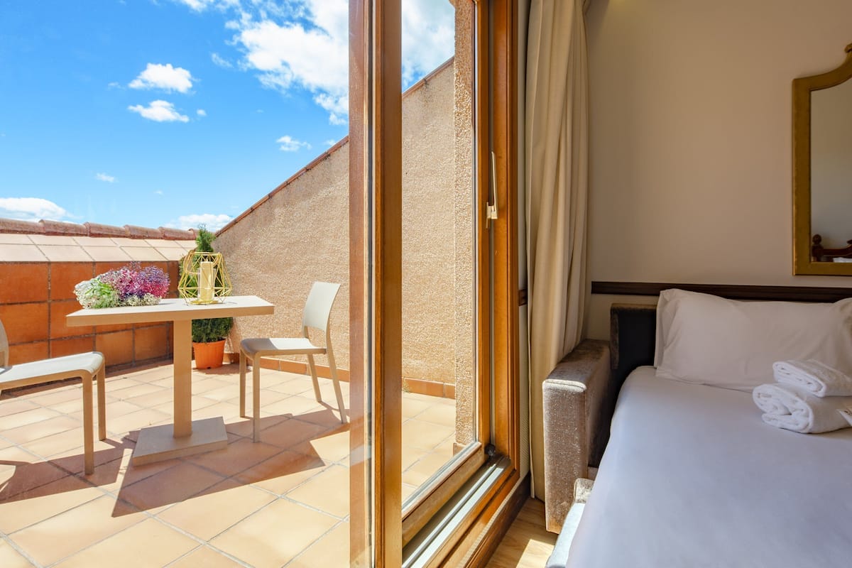 Ein Hotelzimmer mit Balkon, einem Bett mit weißer Bettwäsche, einem Tisch mit Stühlen und einer Topfpflanze.