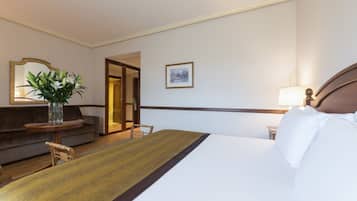 A hotel room with a bed, a sofa, a table with a vase of flowers, a lamp, and a framed picture on the wall.