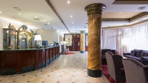 A lobby with a marble column, a reception desk, and a seating area with chairs and sofas. - Dorma Reina Isabel (Ávila)