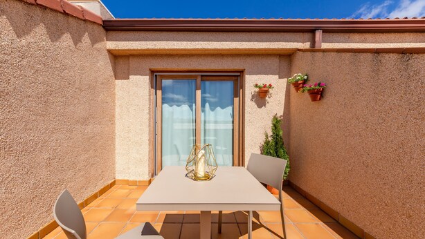 A patio with a table and chairs, a sliding glass door, and potted plants. - Dorma Reina Isabel (Ávila)