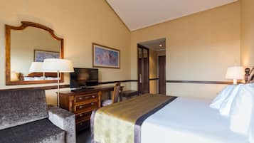 Habitación de hotel con cama, escritorio con televisor, cómoda, silla, espejo y un cuadro en la pared.