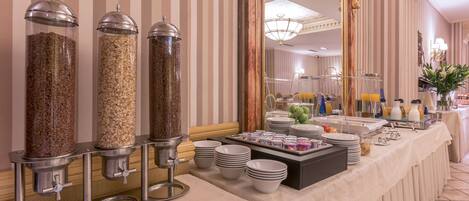 A buffet setup with food dispensers, plates, bowls, and a mirror reflecting the room's decor.
