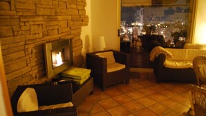 A living room with a fireplace, wicker furniture, and a view of a cityscape at night. - Casa Patronale Tipica Siciliana Home B&B TreMetriSoprailCielo camere con vista, colazione terrazzo panoramico (Caltagirone)