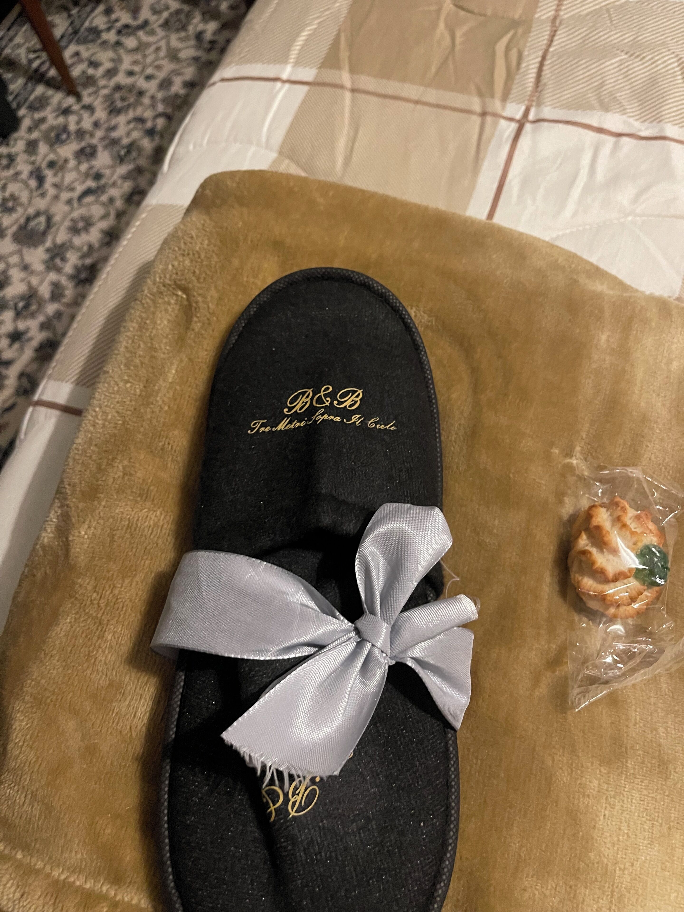 A black slipper with a white ribbon bow and gold lettering on a beige cloth.