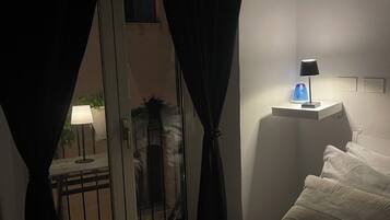 Une chambre d’hôtel avec un lit, une table de chevet avec une lampe et une vue sur un balcon équipé d’une table et de chaises.