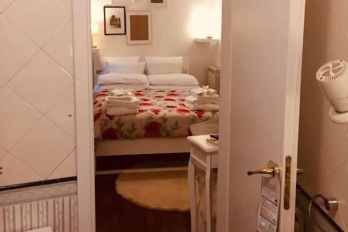 Quarto de hotel com uma cama, mesas de cabeceira, uma pequena escrivaninha e uma porta para um banheiro.