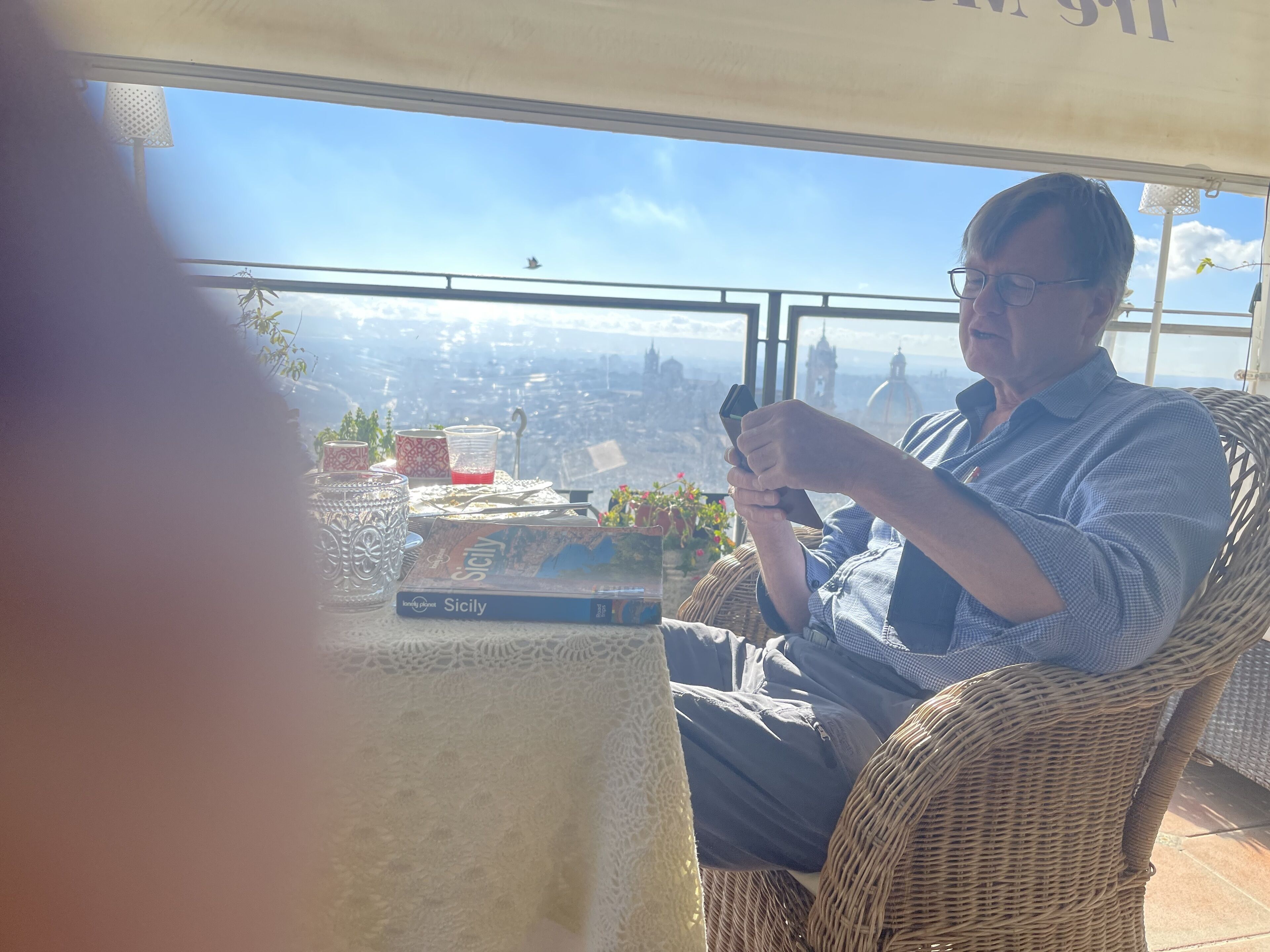 Una persona seduta su una sedia di vimini con vista sulla città attraverso una finestra.