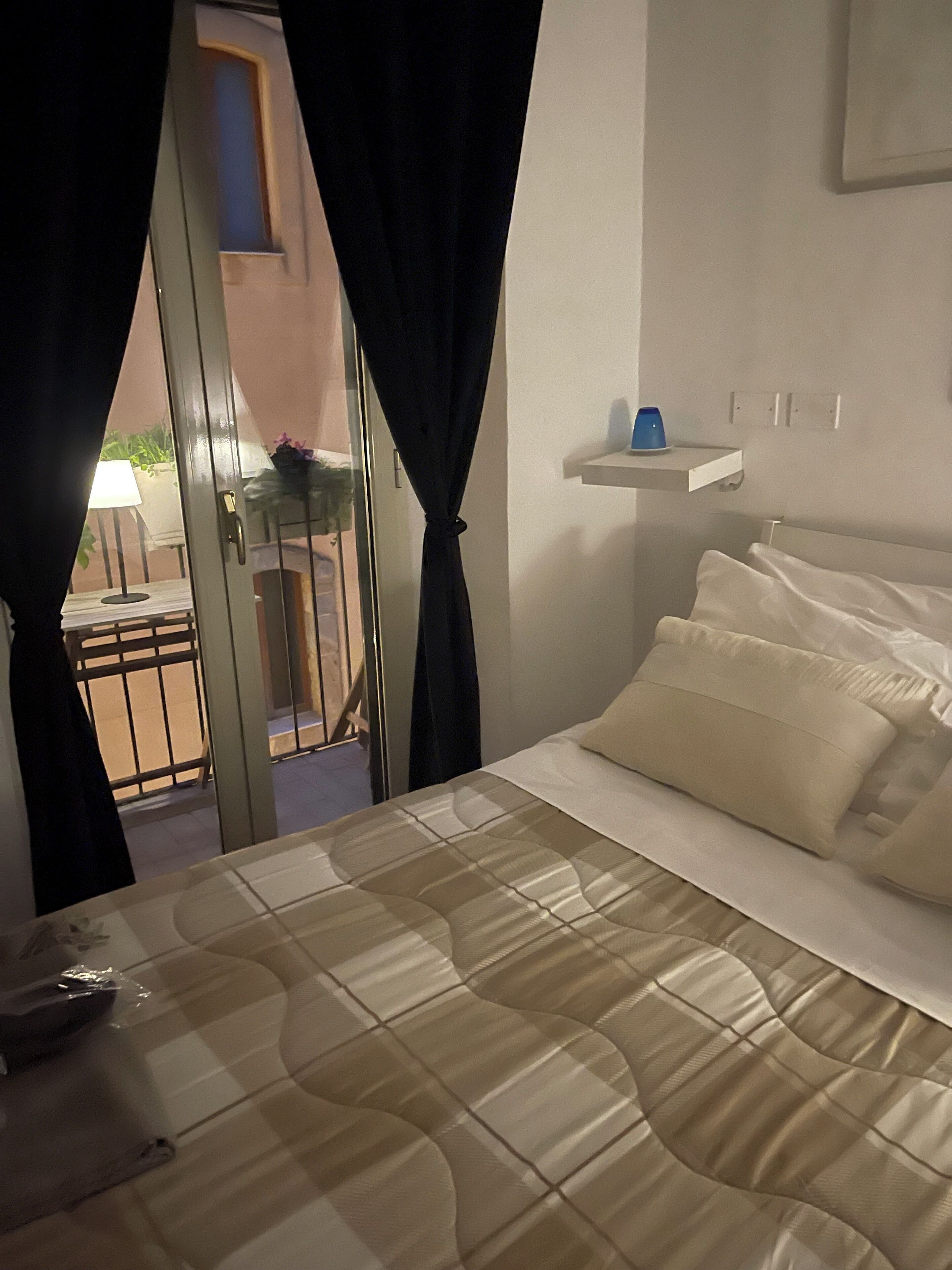 Camera da letto con un letto, tende, una piccola mensola e vista attraverso una porta.