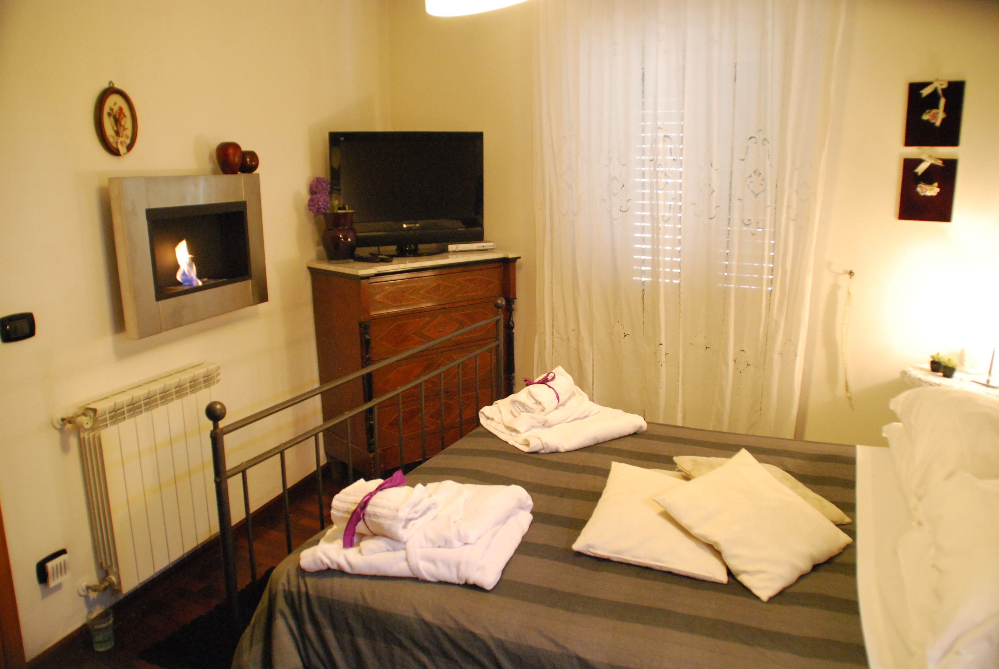 A hotel room with a bed, a flat-screen TV, a fireplace, and a window with curtains.